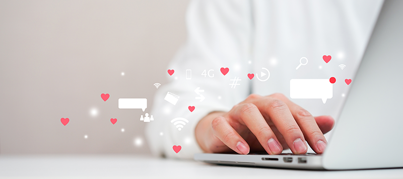 person typing on laptop with social media and heart icons overlayed on the photo